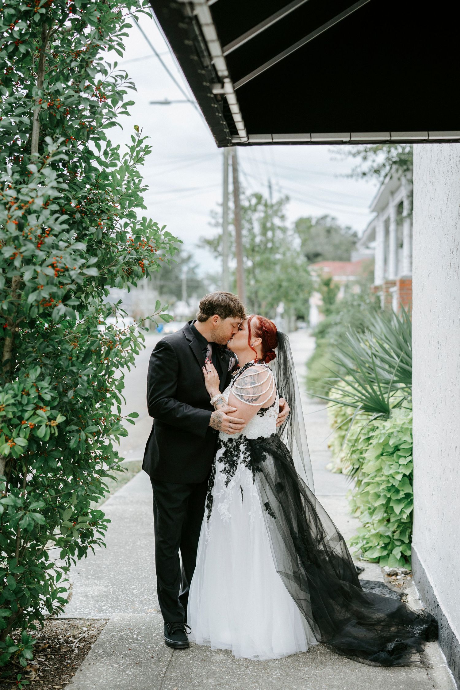 A romantic wedding couple shares a kiss on a garden path with lush greenery and a black and white dress.