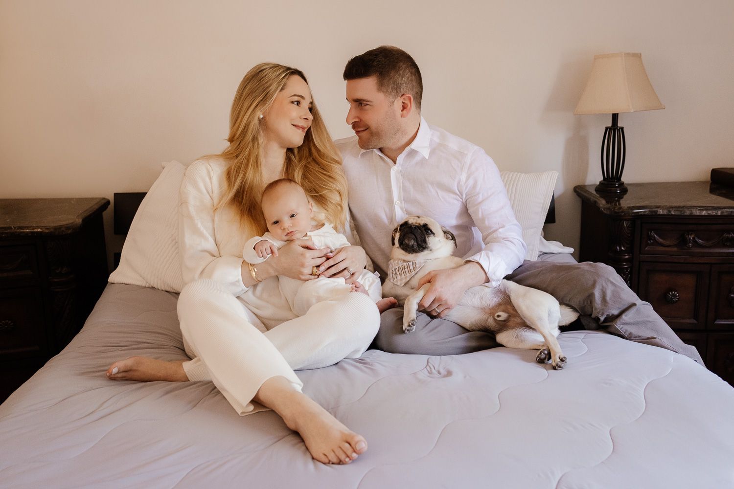 Parents look lovingly at each other as they hold their new baby and dog during a Bay Area newborn photography in-home session