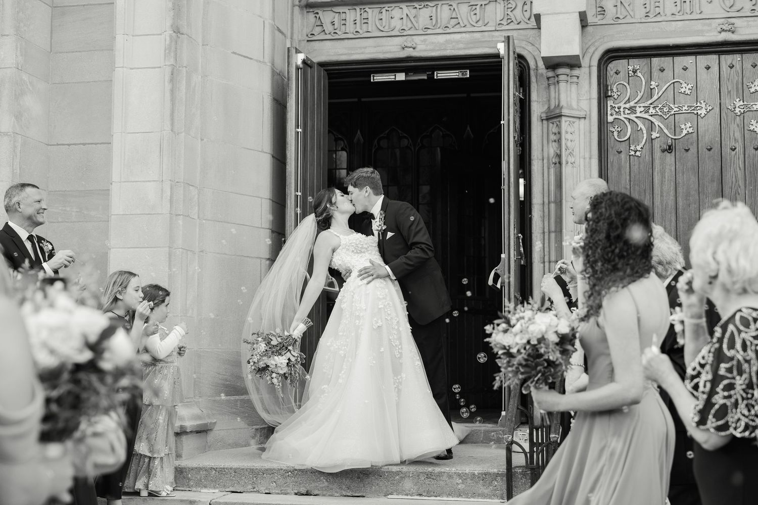 A joyous couple exits a church doorway while wedding guests throw flower petals in celebration on the steps.