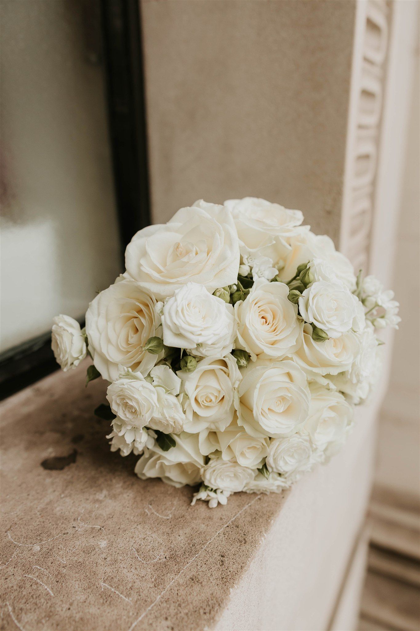 A series of elegant white rose bouquets arranged on a textured beige surface in soft natural lighting.