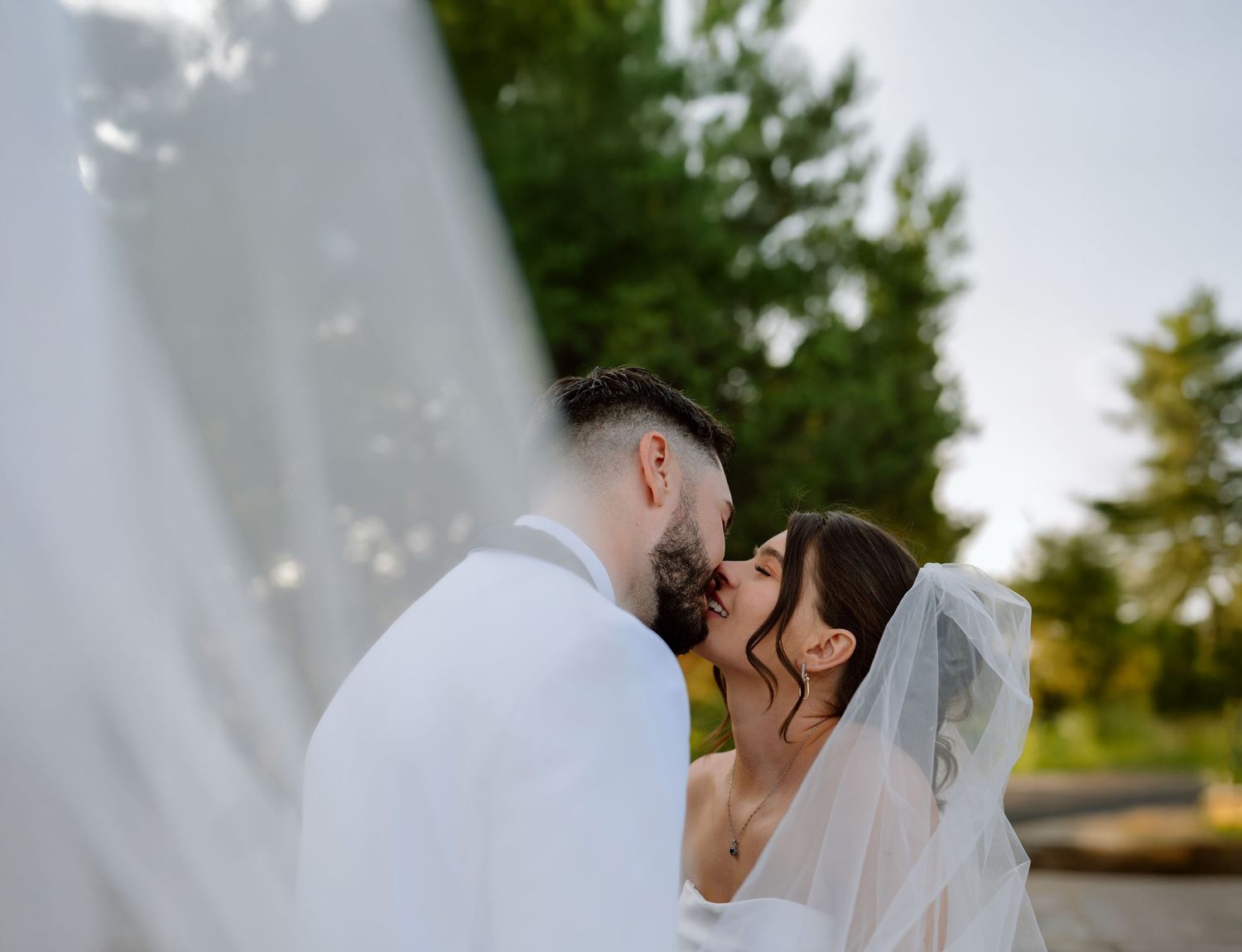 A bride and groom share a romantic kiss outdoors during their wedding photo session.