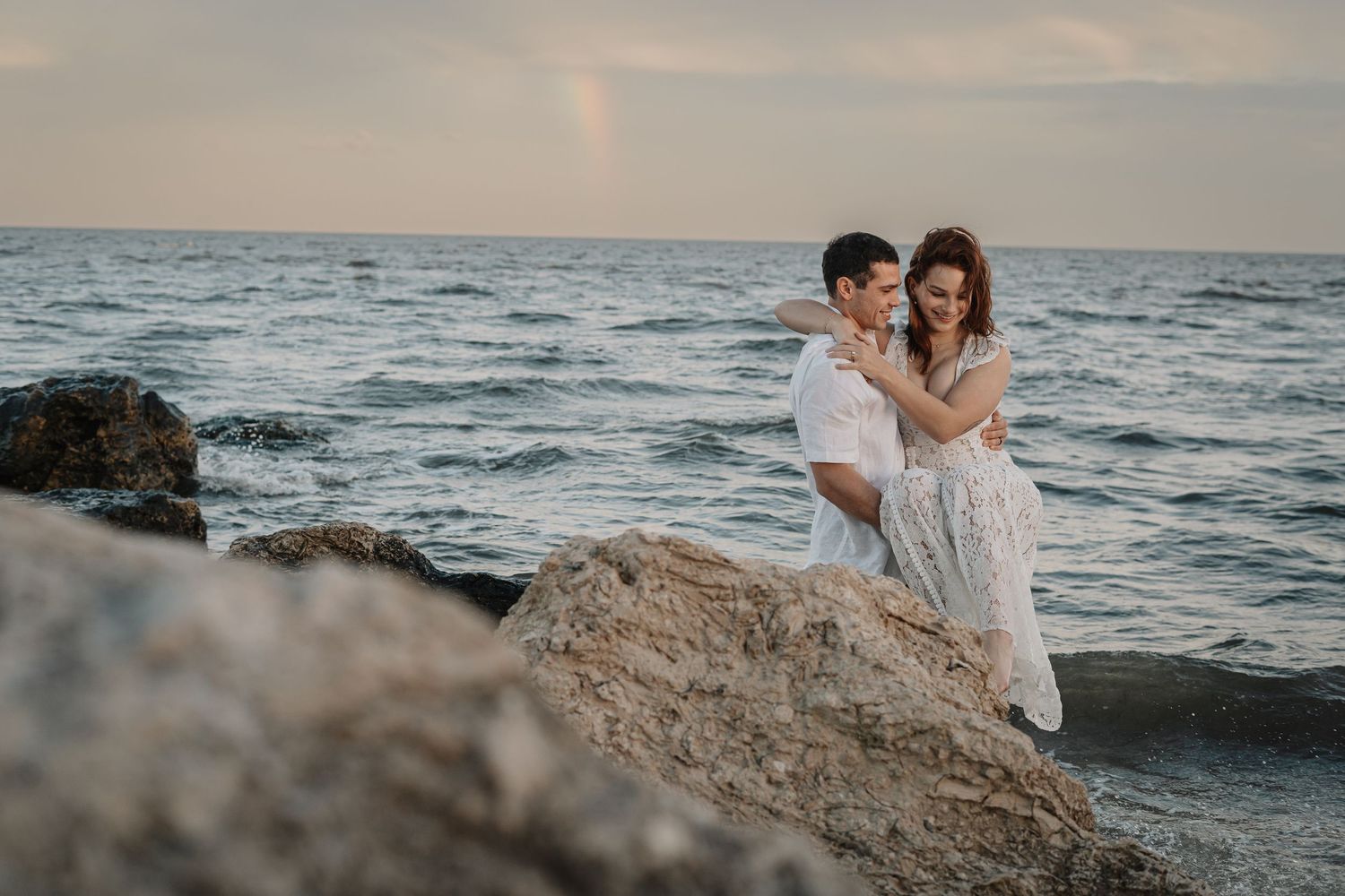A romantic moment between newlyweds under a veil at sunset by a serene lake.