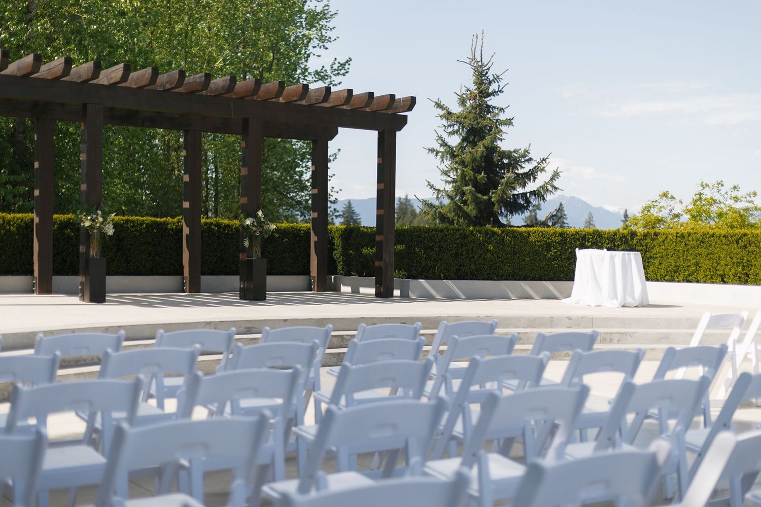 Elegant outdoor wedding ceremony venue with white chairs and pergola altar under blue sky.