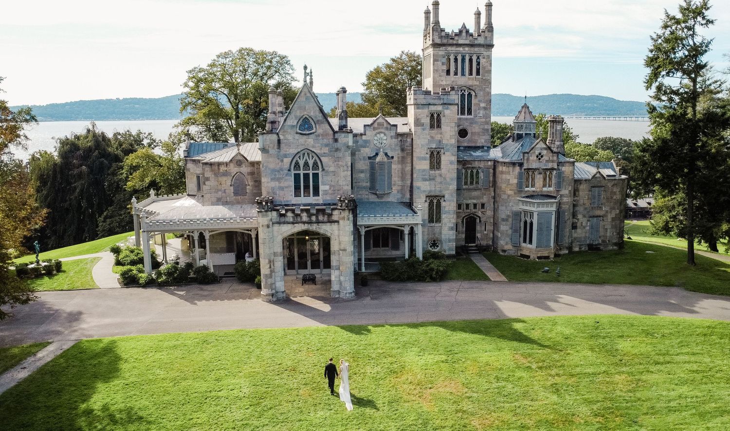 Panoramic view of a Gothic Revival castle with multiple stone towers and turrets overlooking a scenic waterfront landscape.