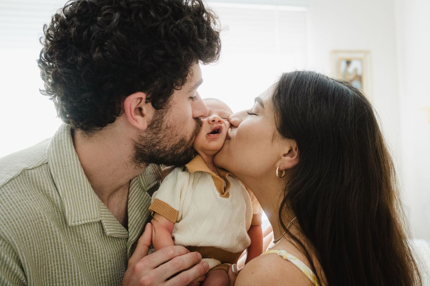 A couple shares an intimate moment sitting together in a bright white nursery room with floral bedding.