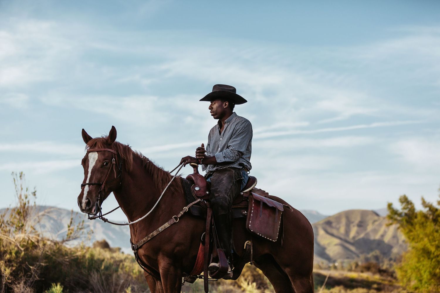 A rider on horseback navigates through scenic desert terrain with mountains in the background under blue skies.