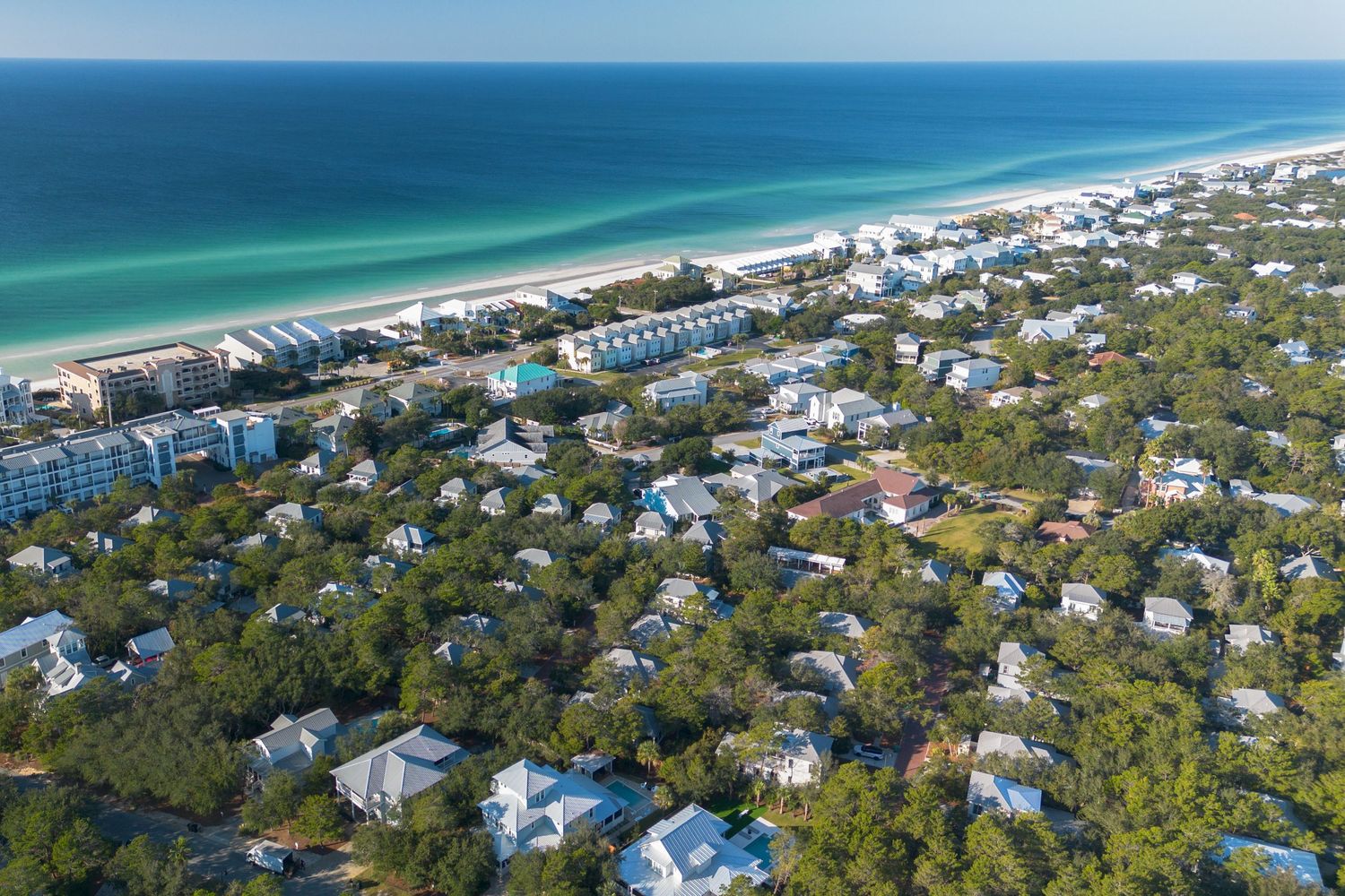 Aerial panoramic view of a coastal beach town with turquoise waters, white sand beaches, and lush green trees.