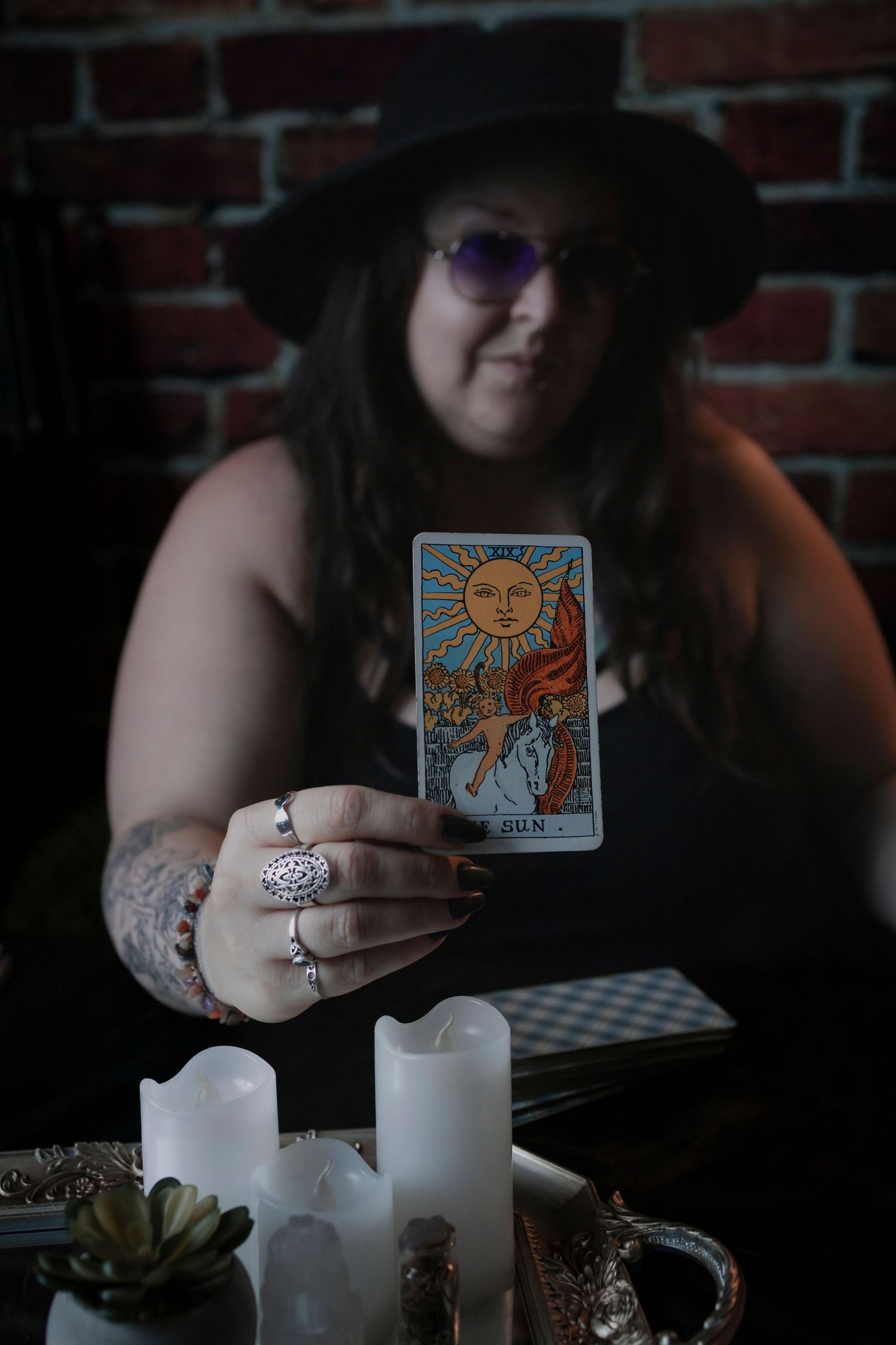 A series of moody photos showing hands using tarot cards and white candles on a dark table with a brick wall background.