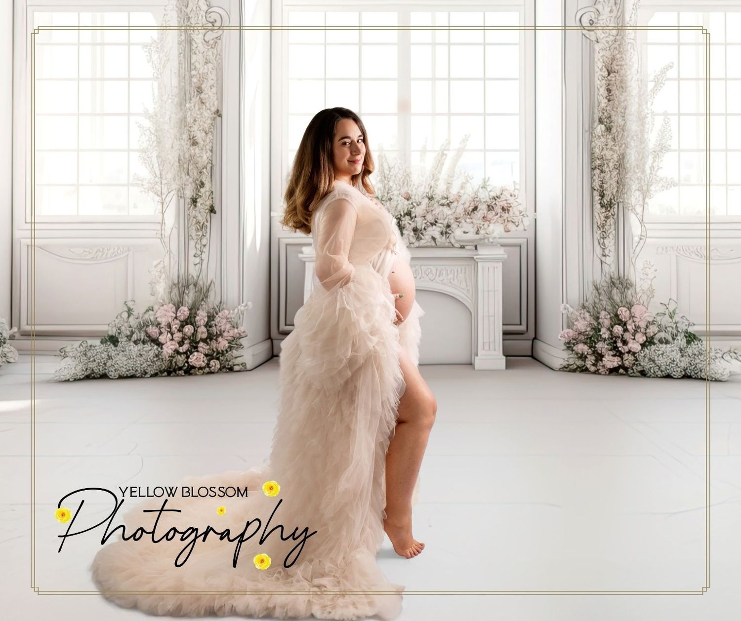 A maternity photo session in an elegant white room with floor-to-ceiling windows and floral decorations.