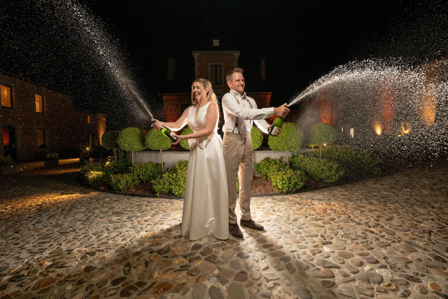 Wedding couple stand together as sparklers illuminate the stone pathway at their romantic outdoor nighttime celebration.