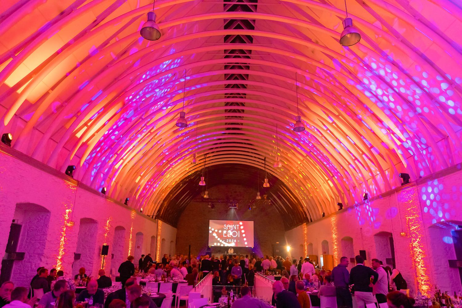 Vibrant pink and purple lighting illuminates a wedding reception venue with curved architecture and elegant decor.