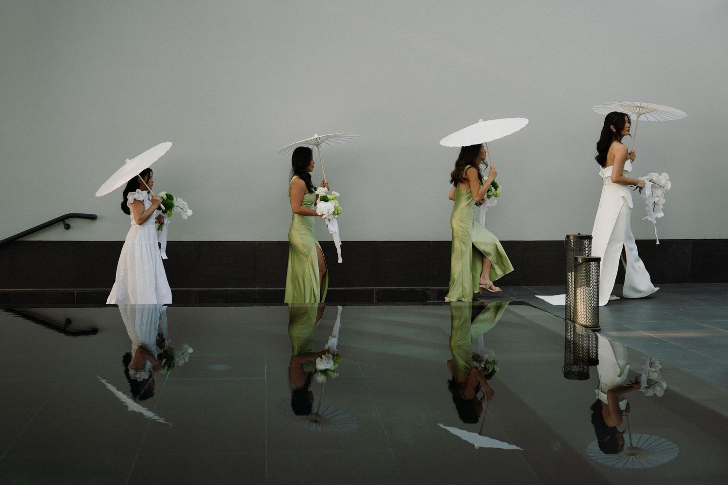 A sequence of dance performers in white and green costumes moving across a dark stage in synchronized motion.