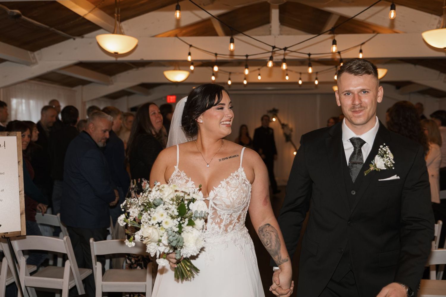 Joyful newlyweds walking down the aisle after wedding ceremony in bright white reception venue.