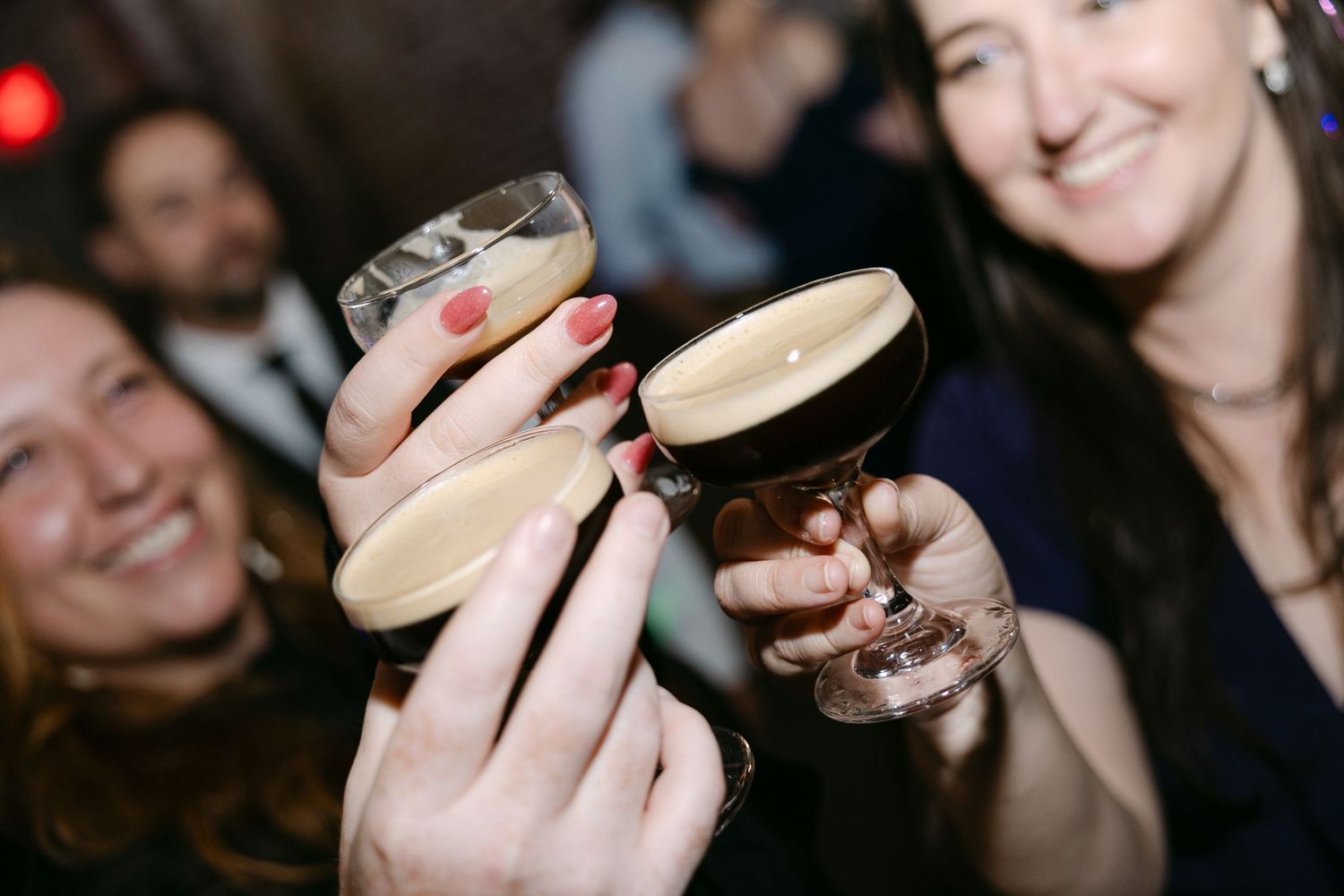 Friends toasting and clinking dark beer glasses together in a dimly lit bar setting.