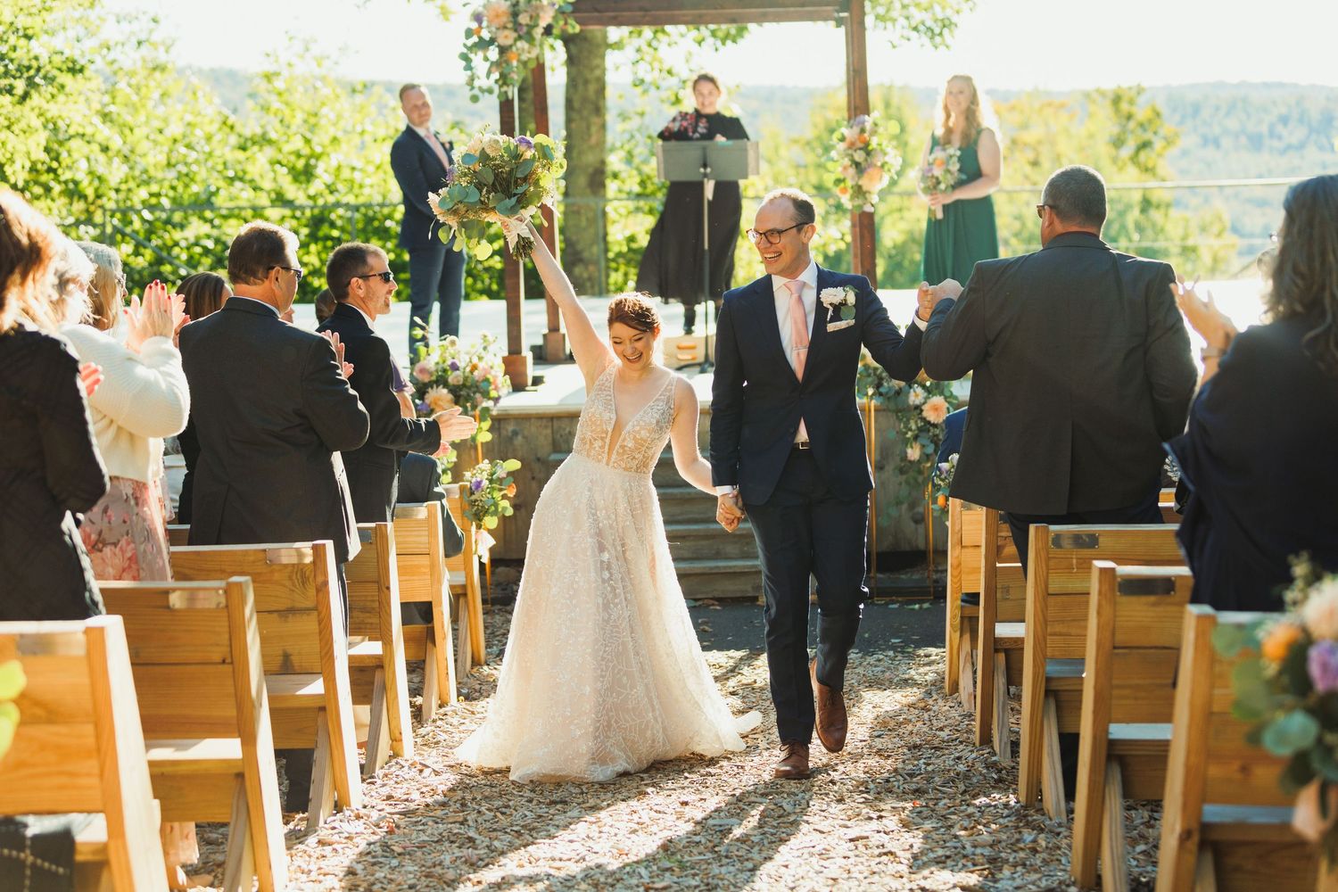 Outdoor wedding ceremony setup with wooden chairs and a covered pavilion in a scenic mountain setting.