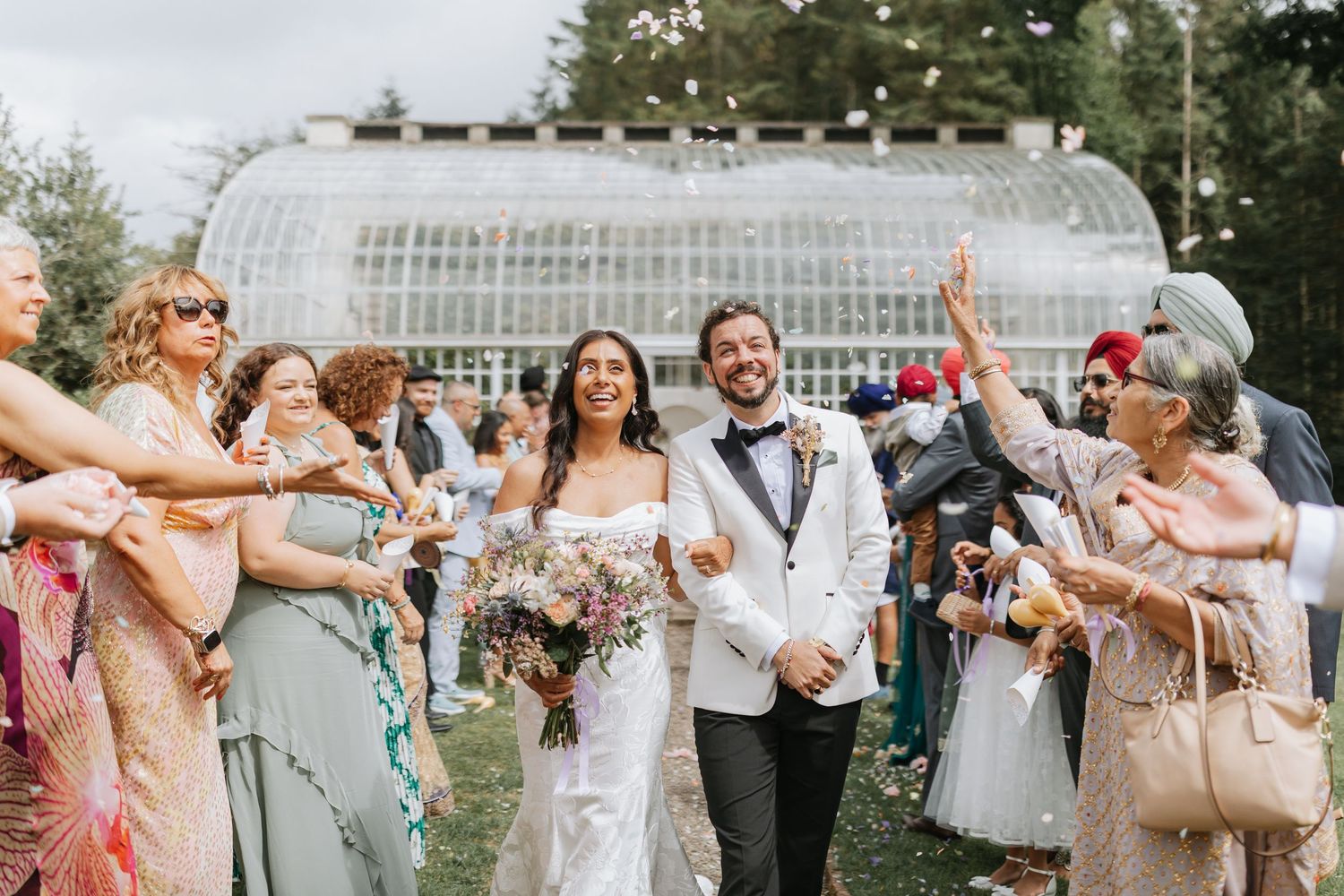 Wedding guests celebrate and dance together during an outdoor reception party in a garden setting. Hopton Court Wedding Venue.