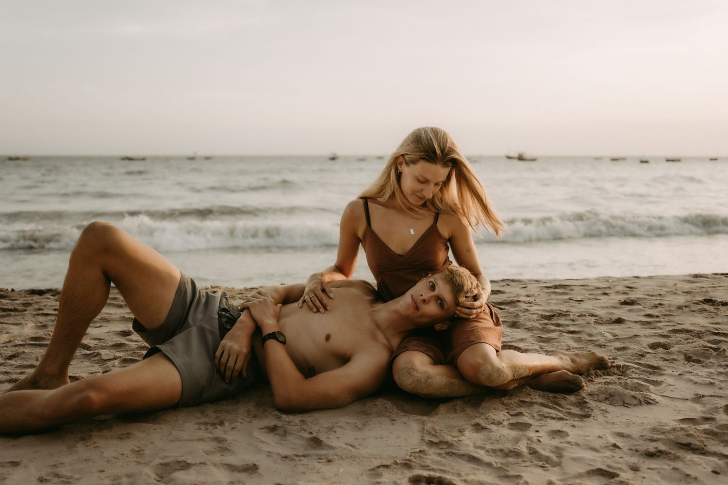 A couple relaxes together on a sandy beach at sunset creating romantic silhouettes against the ocean waves.