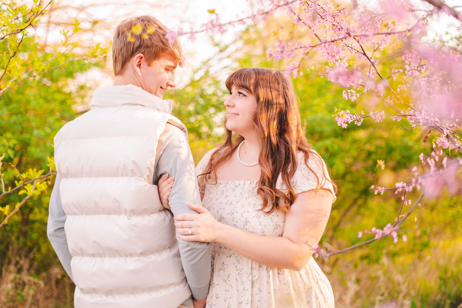 A couple embraces under blooming pink cherry blossom trees during a romantic outdoor engagement session.