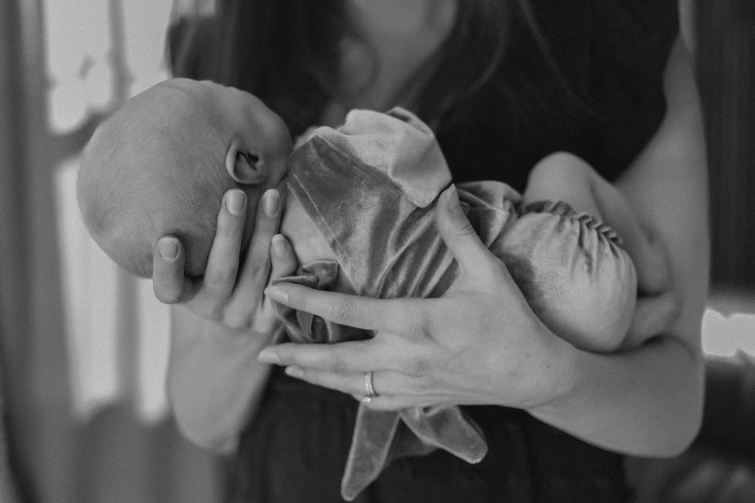 A black and white photo of a newborn baby being cradled in gently in mothers arms.  The focus is mothers hands cradling the baby.