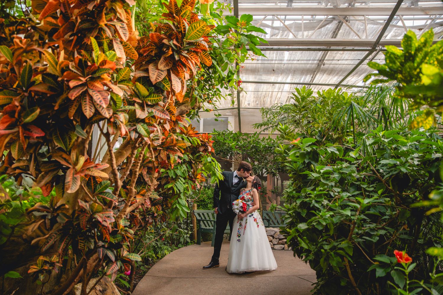 Wedding couple standing in a lush greenhouse surrounded by tropical plants and flowers.