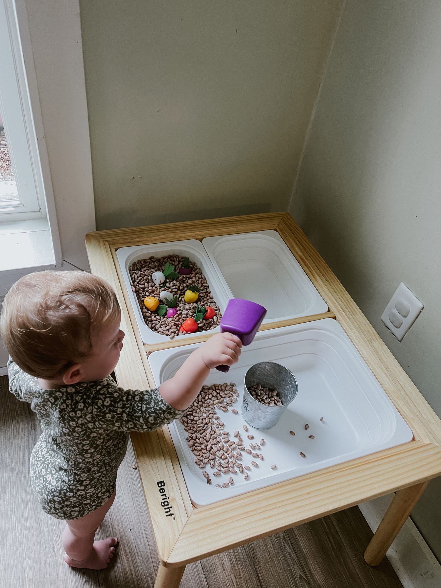 12 month old baby doing a sensory table activity using her Flisat and Bright table  beans, carrots, fruits, and veggies