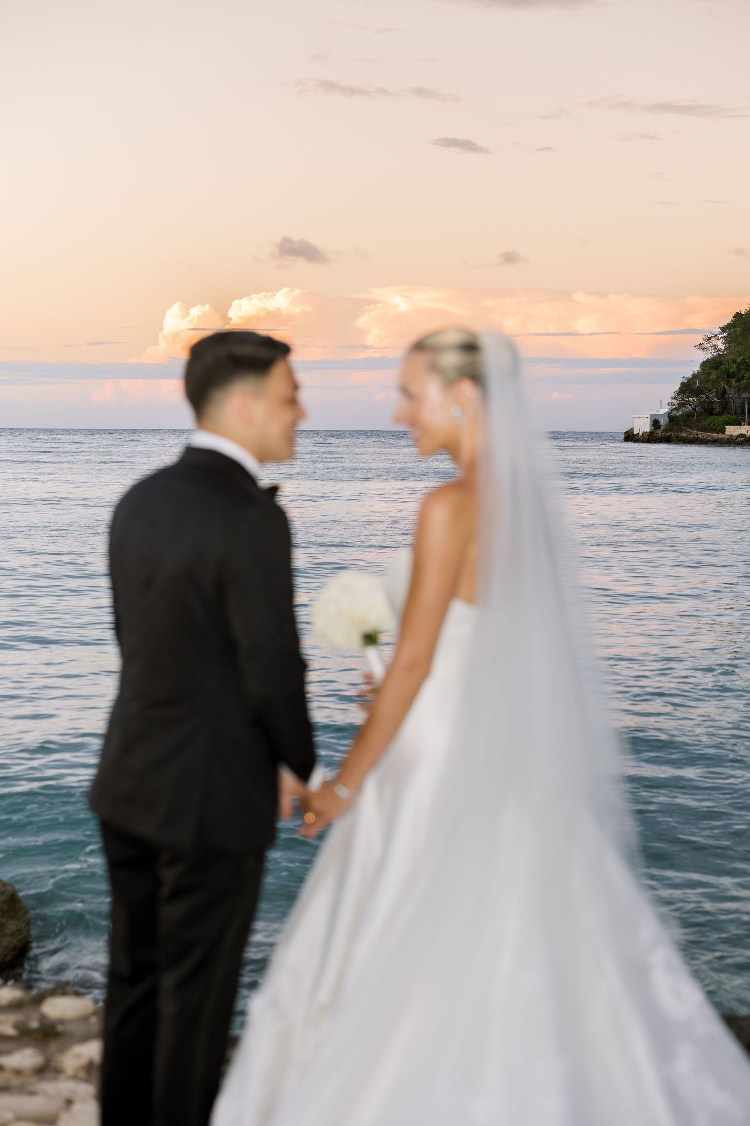 Bride and groom share a romantic kiss by the ocean at sunset. Round Hill Jamaica wedding