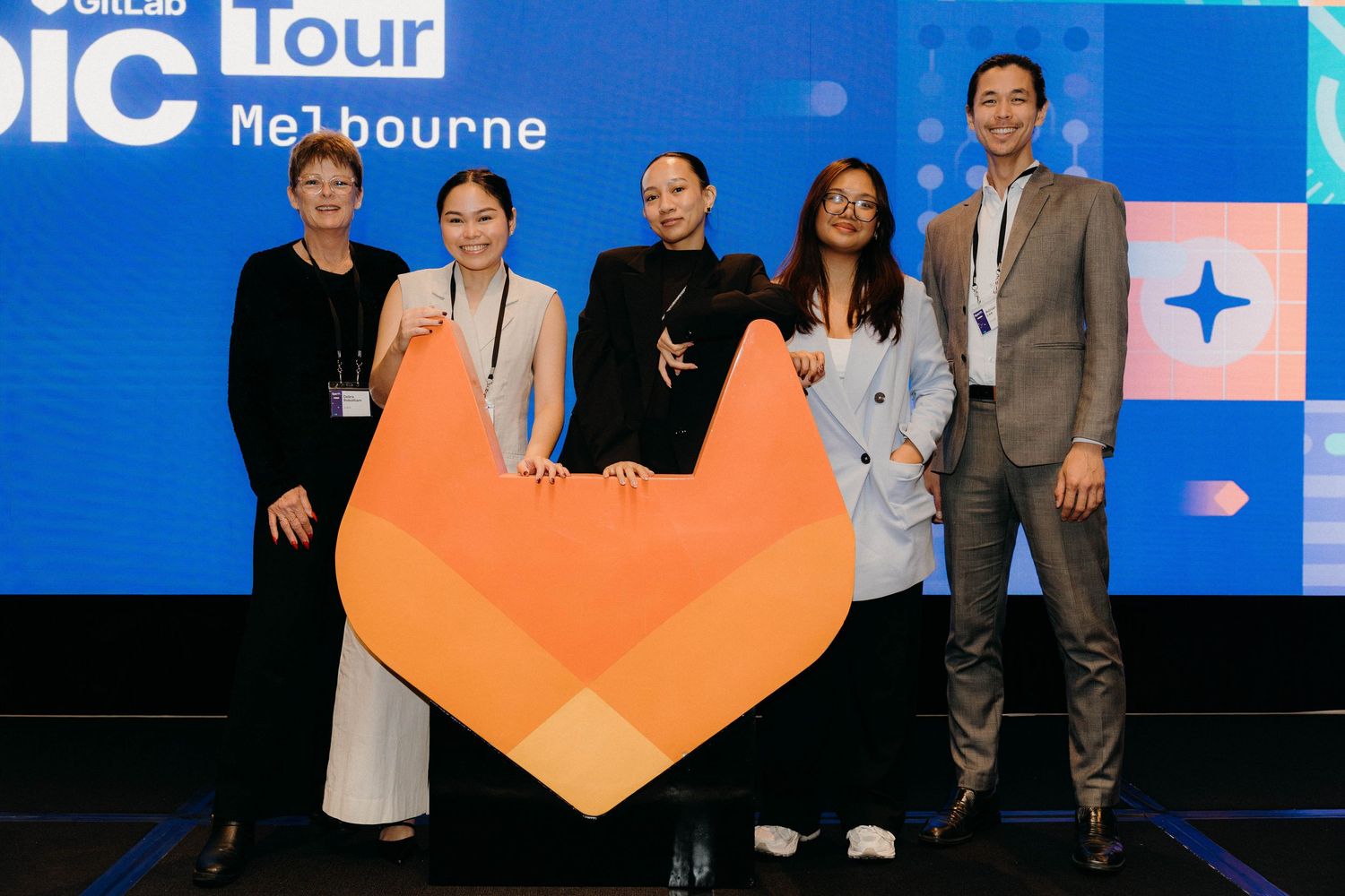 Five professionals pose with GitLab fox logo at GitLab Epic Tour Melbourne event on stage.