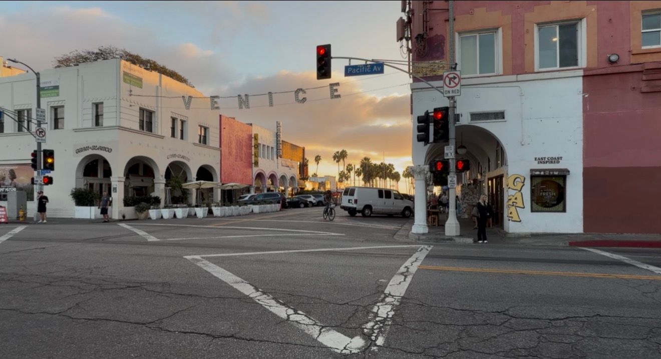 Quiet Venice Beach intersection at sunset with a Venice sign, traffic lights, palm trees, and historic arcade buildings in Los Angeles.