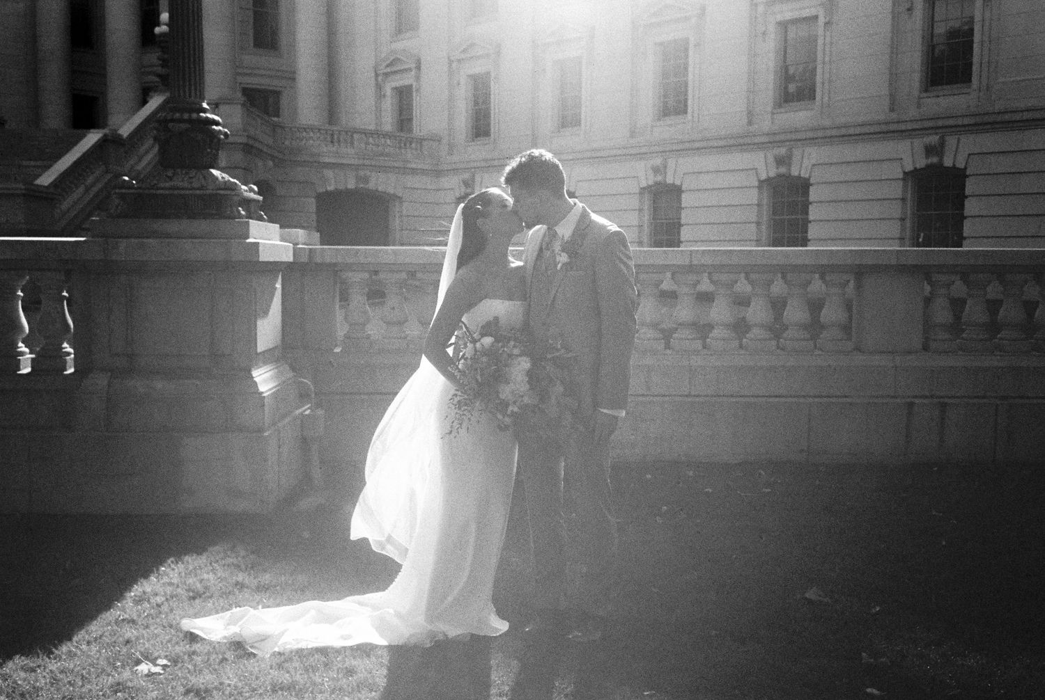 Dancing couple surrounded by elegant white pillars and grand wooden doors of a historic government building.