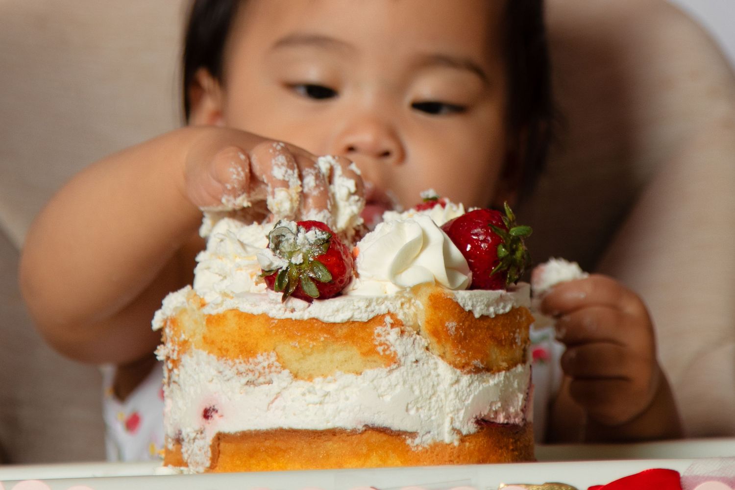A young child eating a colorful cake with whipped cream and strawberries.