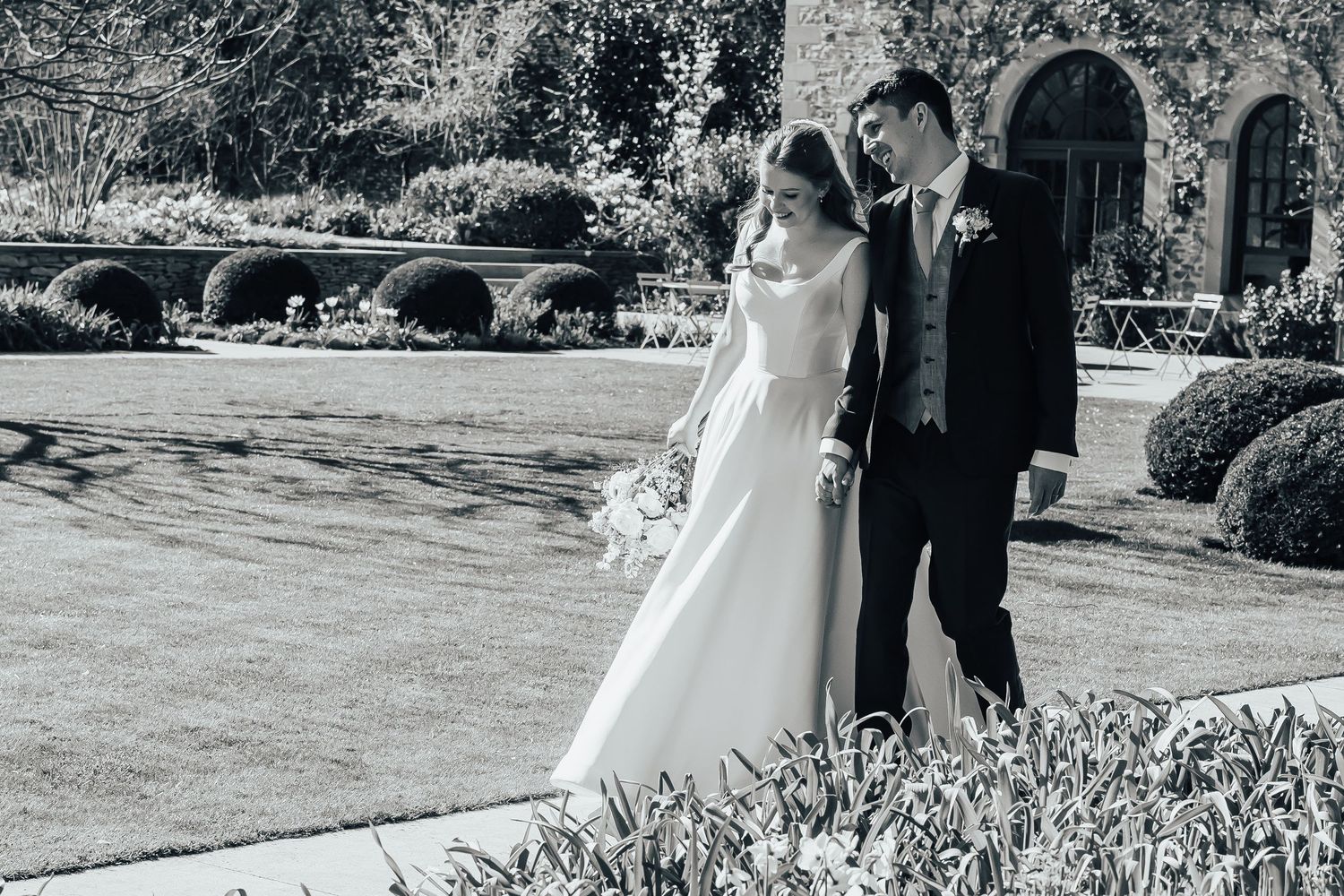 Elegant outdoor wedding venue with floral arch of white roses leading to glass-doored orangery surrounded by lush greenery.
