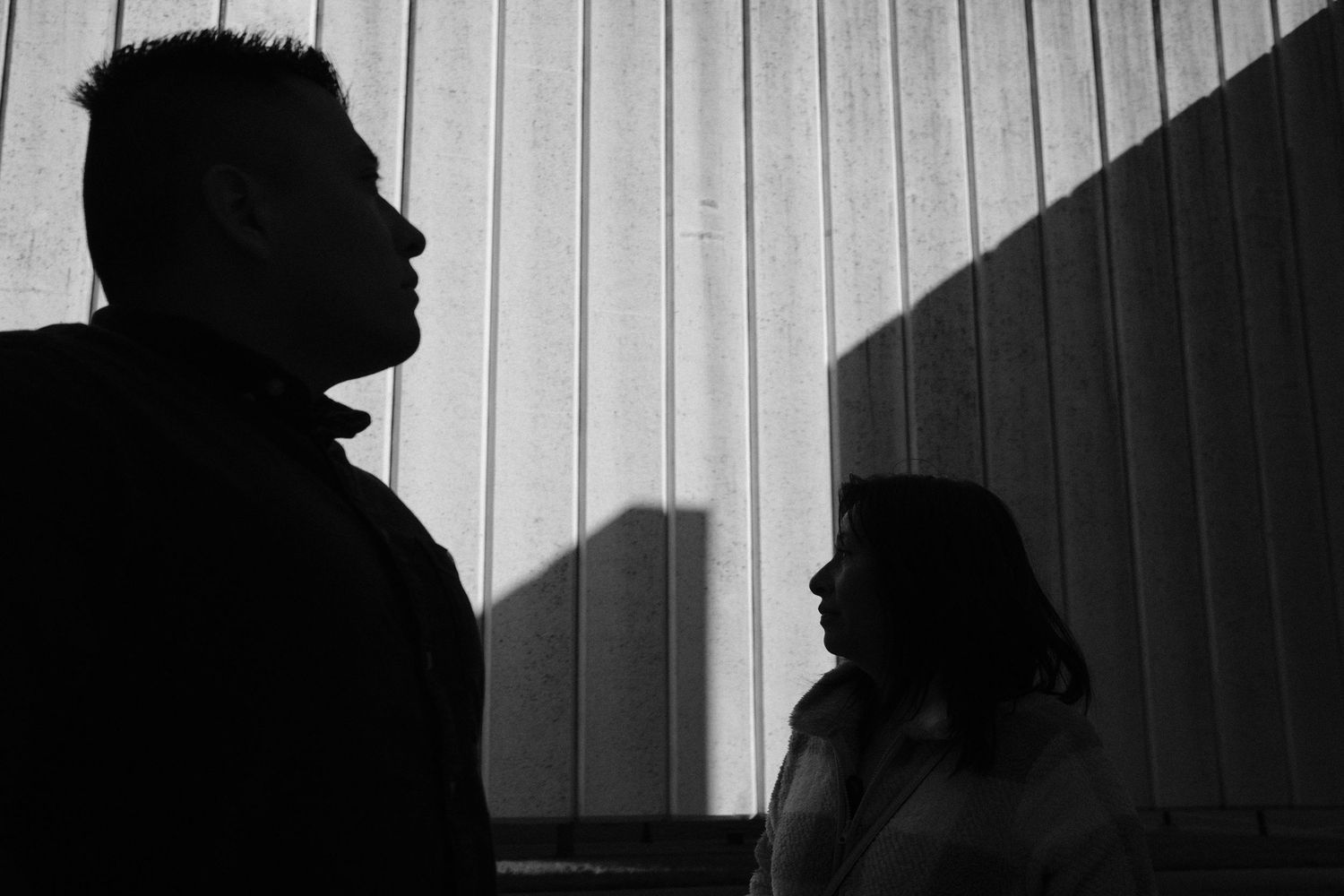 Black and white silhouette of a man and woman standing together with dramatic shadows on a striped wall.
