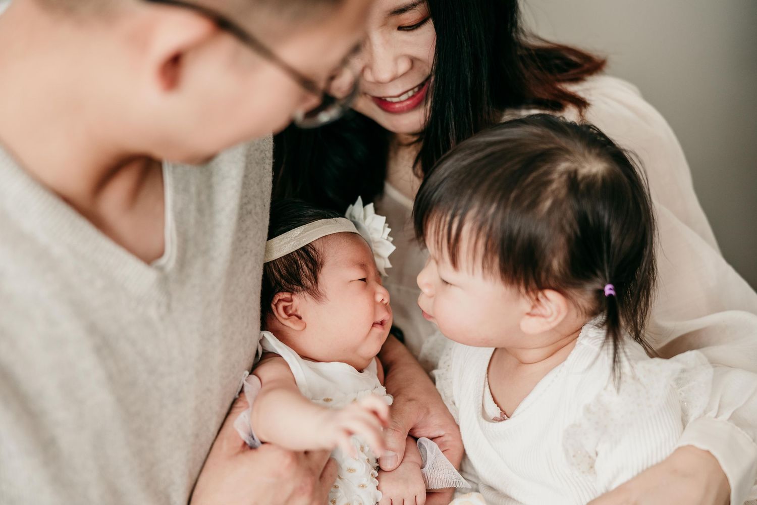 Smiling Asian family admiring newborn baby as toddler sibling leans in for a closer look.