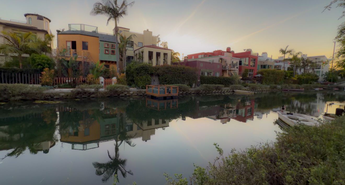 Scenic panoramic view of waterfront homes along a tranquil canal at sunset with palm trees and reflections on calm water.