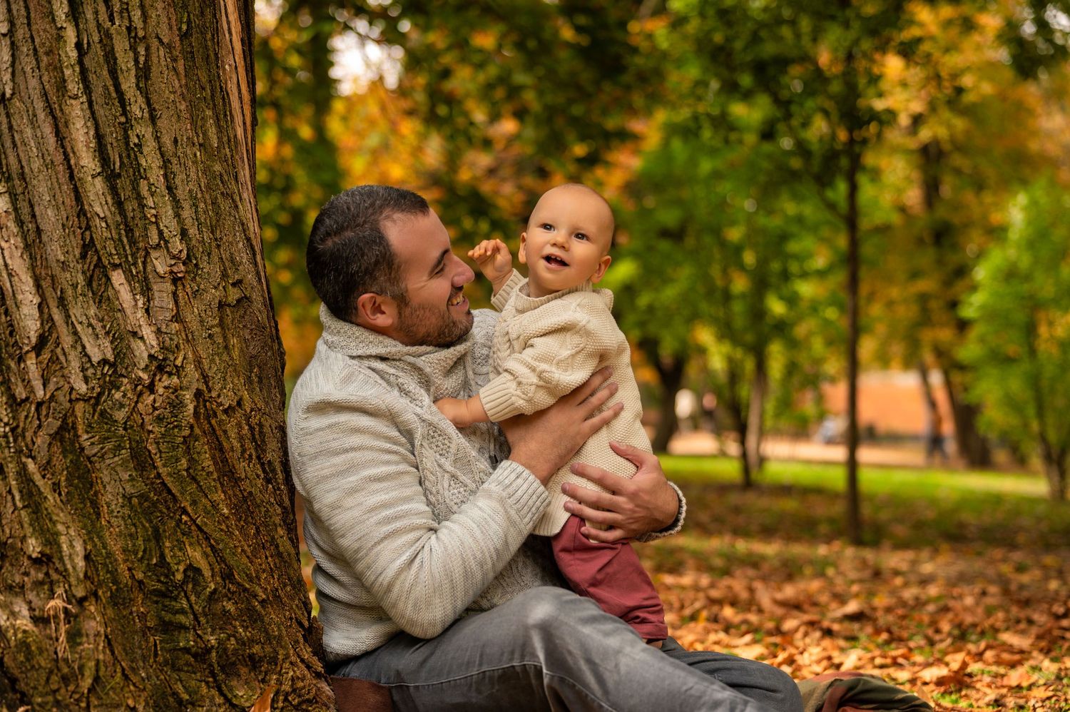 Two people share a tender moment among autumn leaves in a park setting during golden hour.