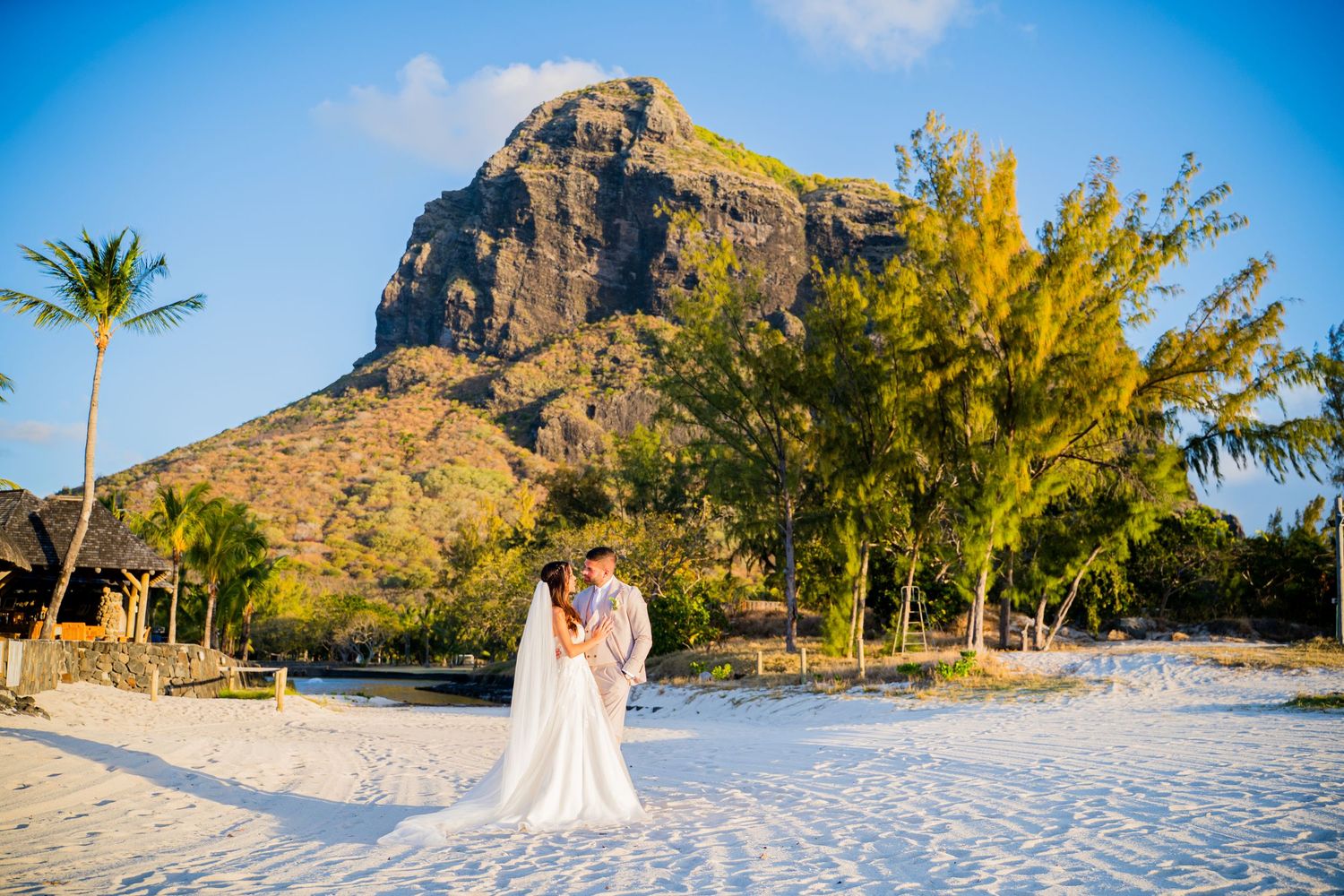 Couple walking hand in hand on white sand beach with Le Morne Brabant mountain backdrop in Mauritius.