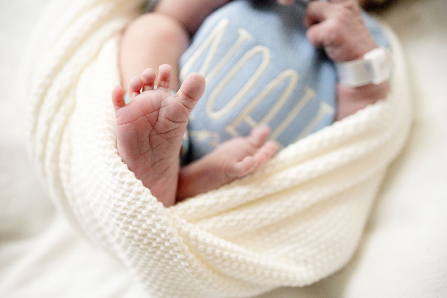 Close-up of newborn baby feet peeking out of a white swaddle blanket in a hospital setting.