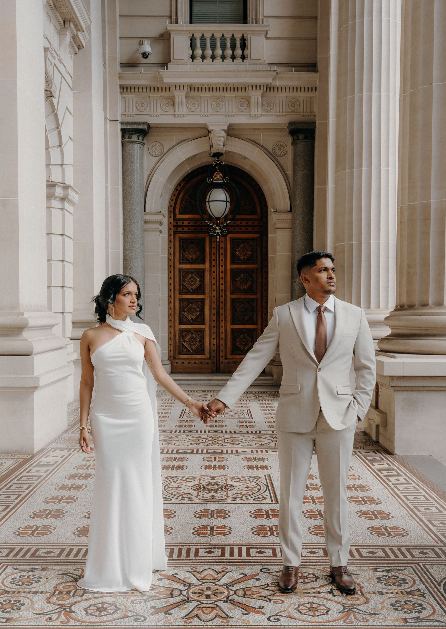 Couple posing on staircase in wedding attire, groom in black suit, bride holding pink bouquet in white dress.