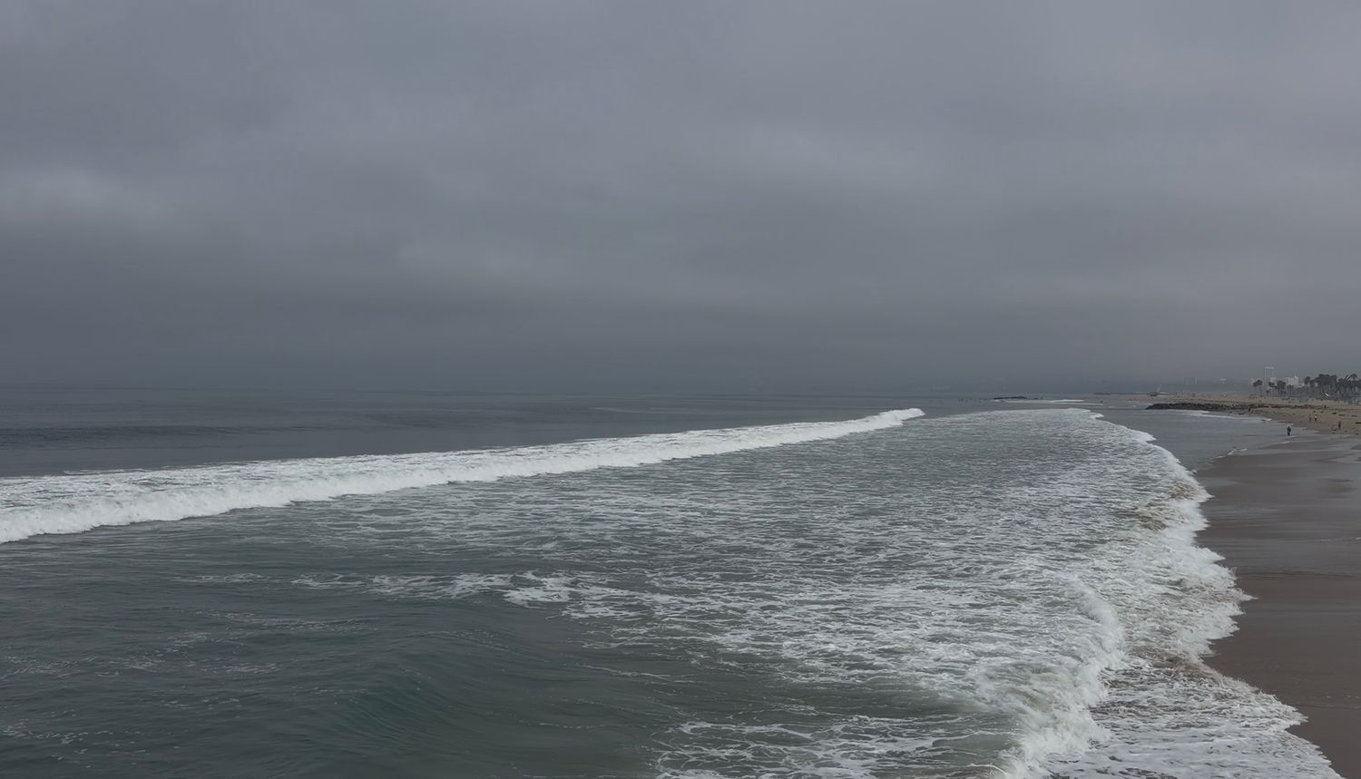 Stormy ocean beach with dramatic gray clouds, rolling waves crashing on sandy shore under overcast skies.