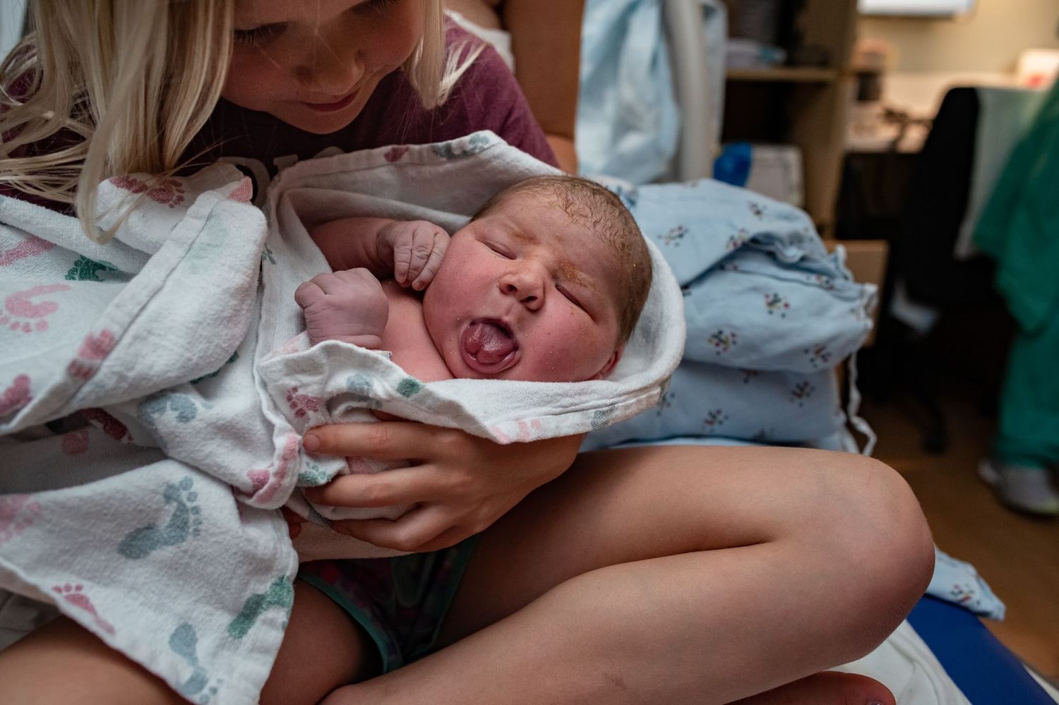 A newborn baby crying while being held in a hospital blanket.