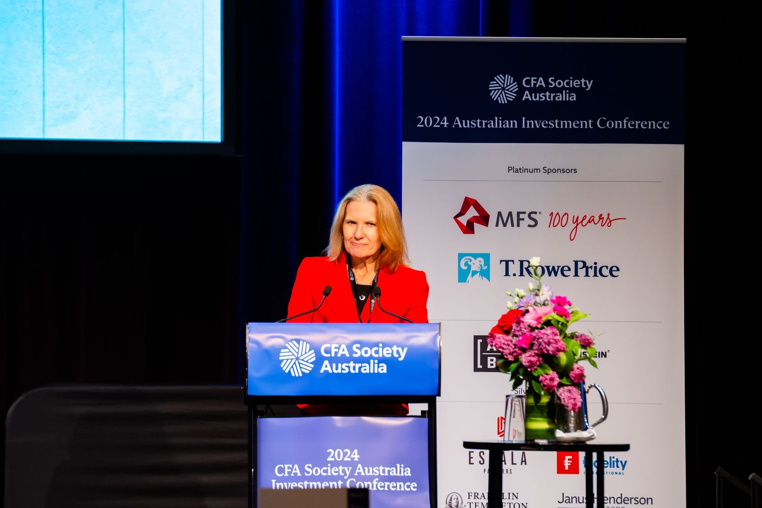 Speaker at the 2024 CFA Society Australia Investment Conference podium with MFS and T. Rowe Price sponsor banners.
