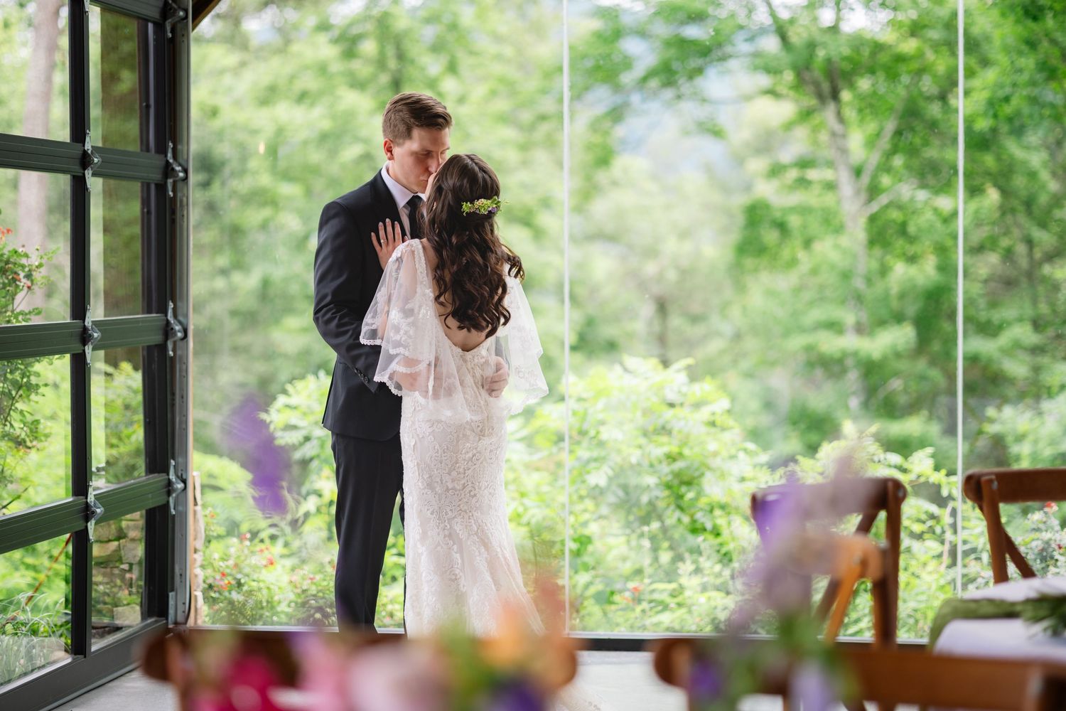 A couple shares their first dance at a wedding reception surrounded by lush greenery and natural light.