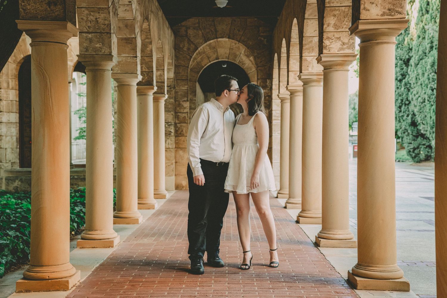 A couple shares an intimate moment under a beautiful columned archway in a garden setting.