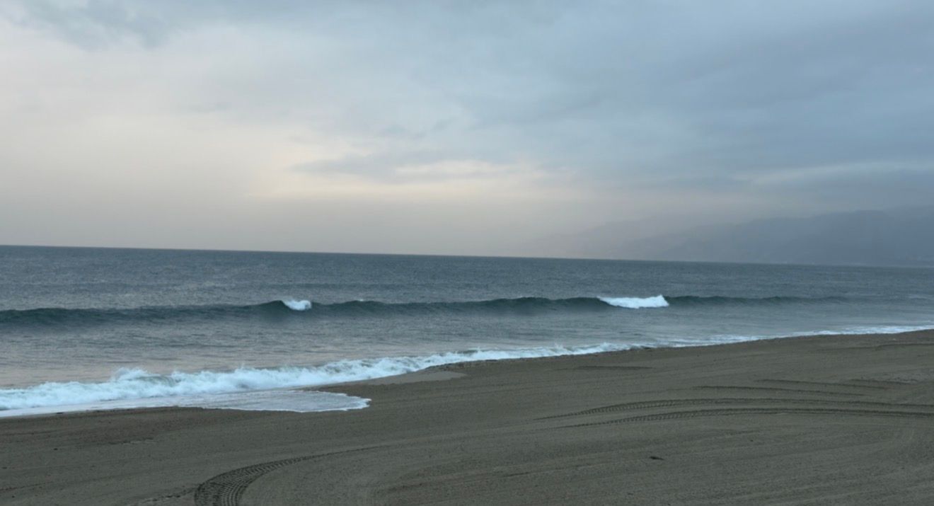 Ocean waves break on a dark sandy beach under an overcast sky during dusk.