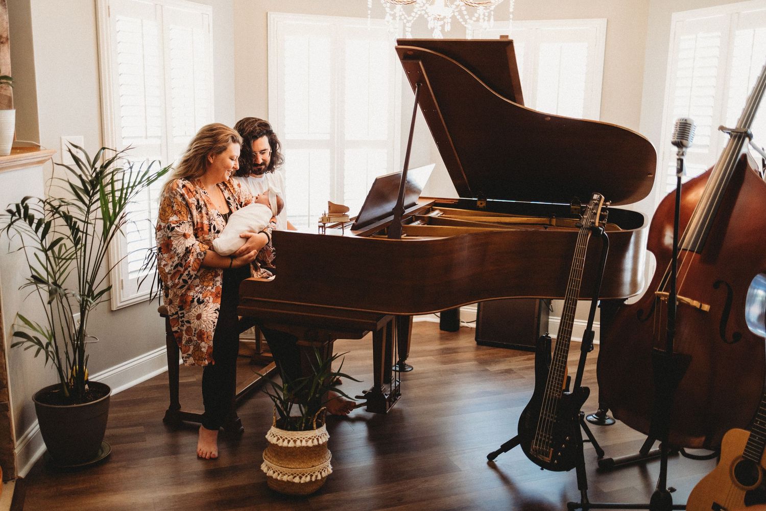 Two women admire a newborn baby near a grand piano in a music room with guitar and cello.