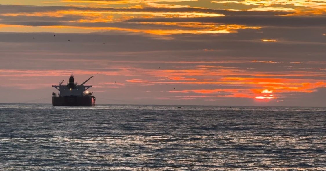 Oil rig silhouette against vibrant orange and pink sunset sky over calm ocean waters.