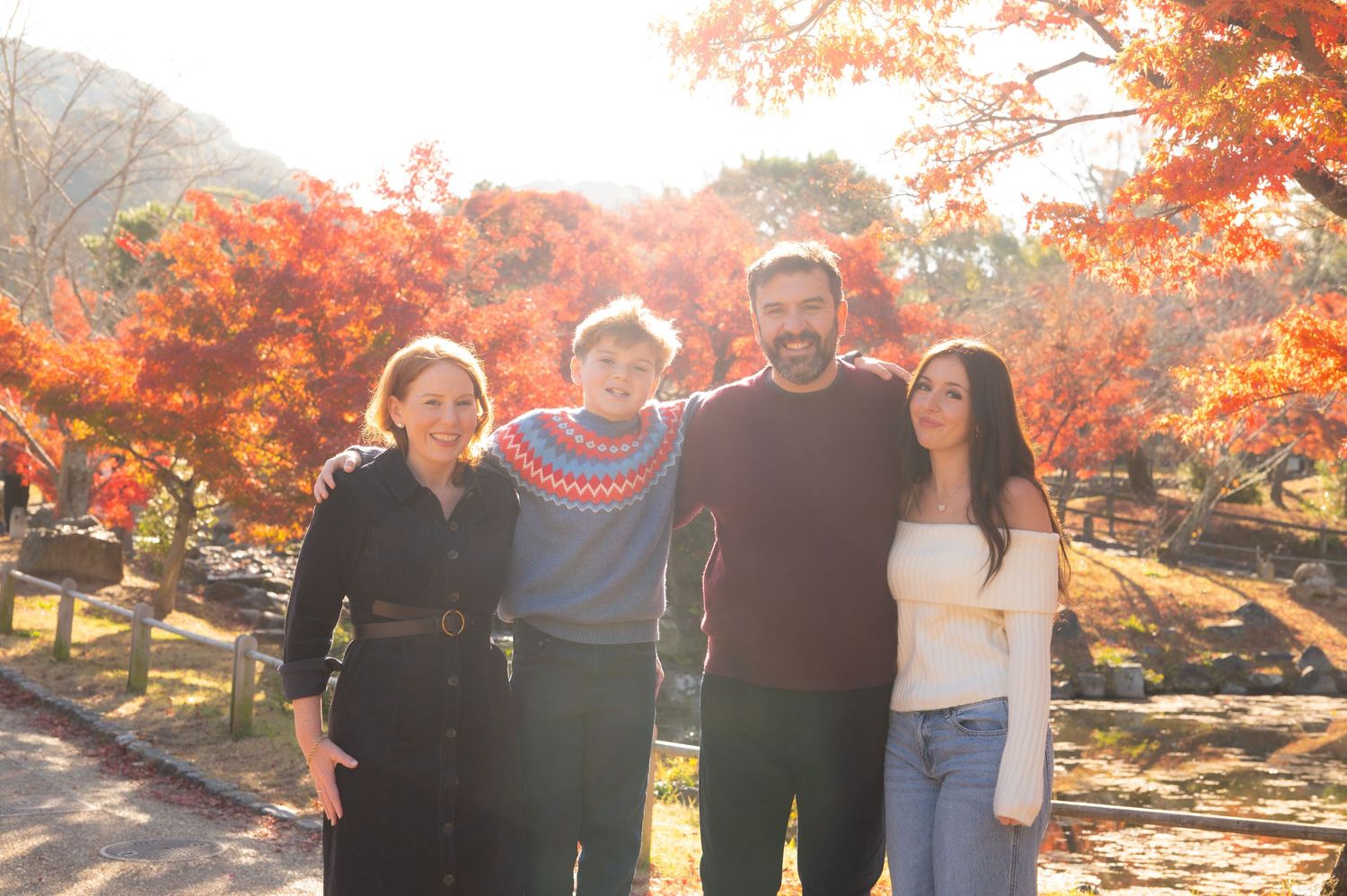 Family of four smiling together surrounded by vibrant red autumn foliage in Japan.