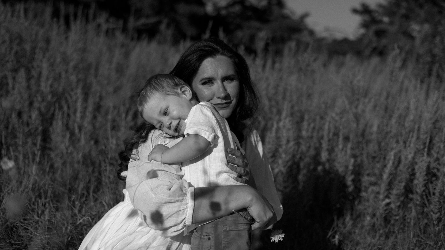 A black and white photo series shows tender moments between a couple and their baby in a natural outdoor setting.
