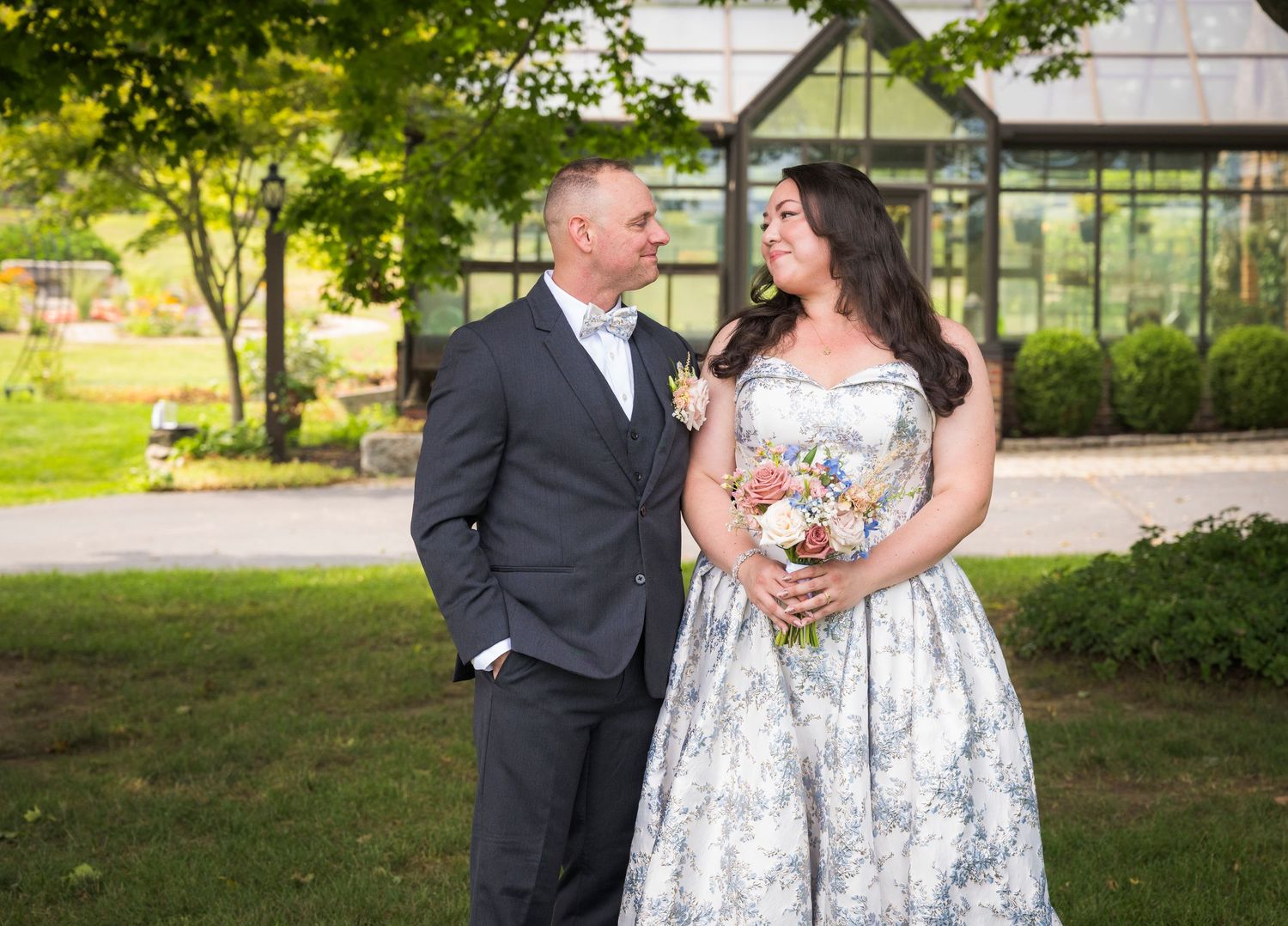 Newlyweds share an intimate moment outdoors with autumn foliage and rustic architecture in background.