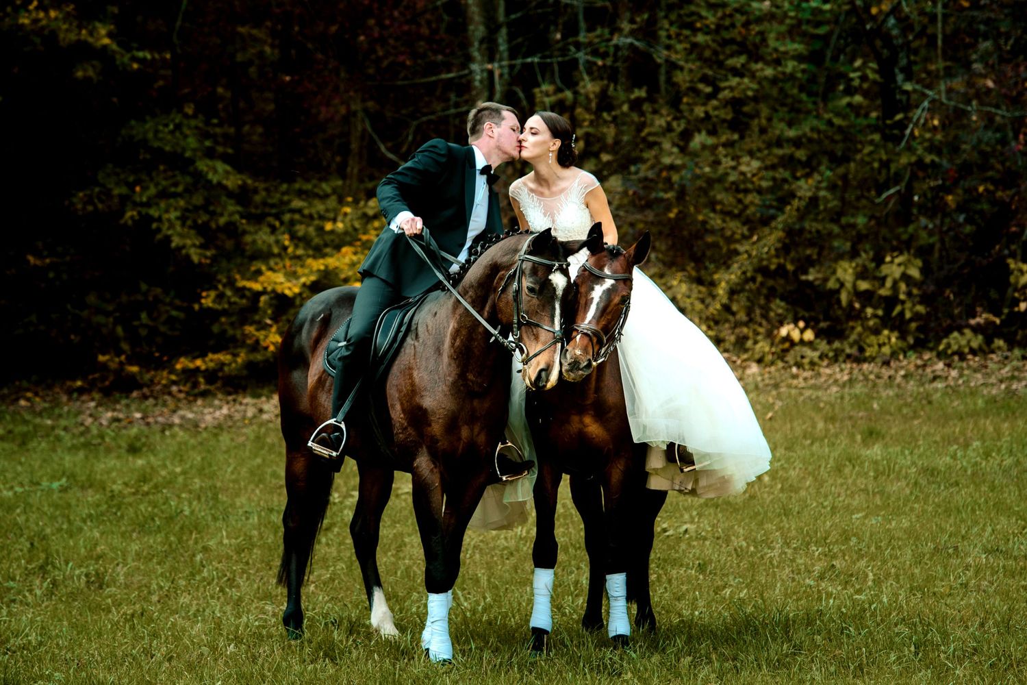 Couple poses with horses in an outdoor wedding photoshoot on grassy field.